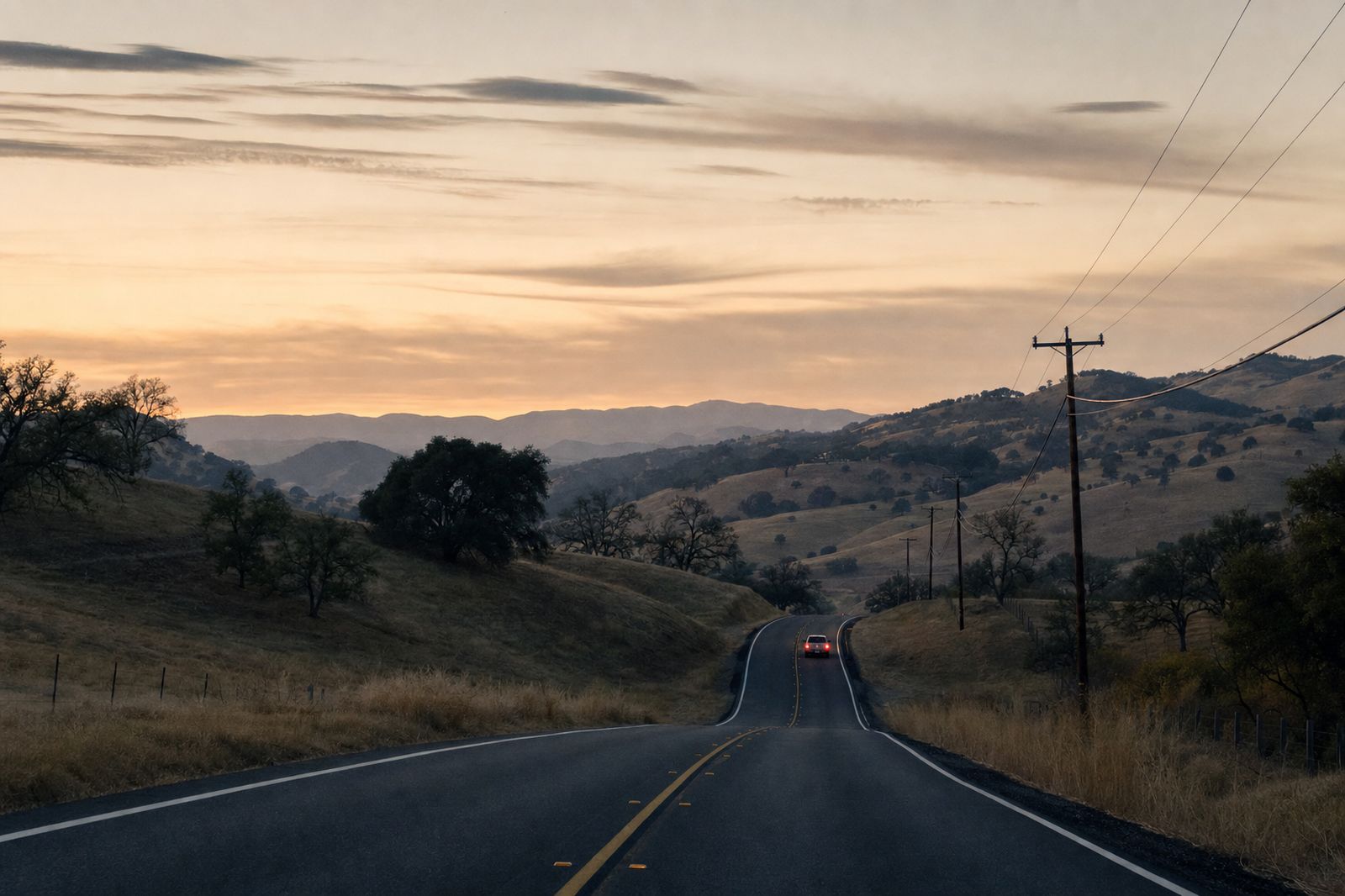 A two-lane highway winding through oak-studded Napa County hills at dusk